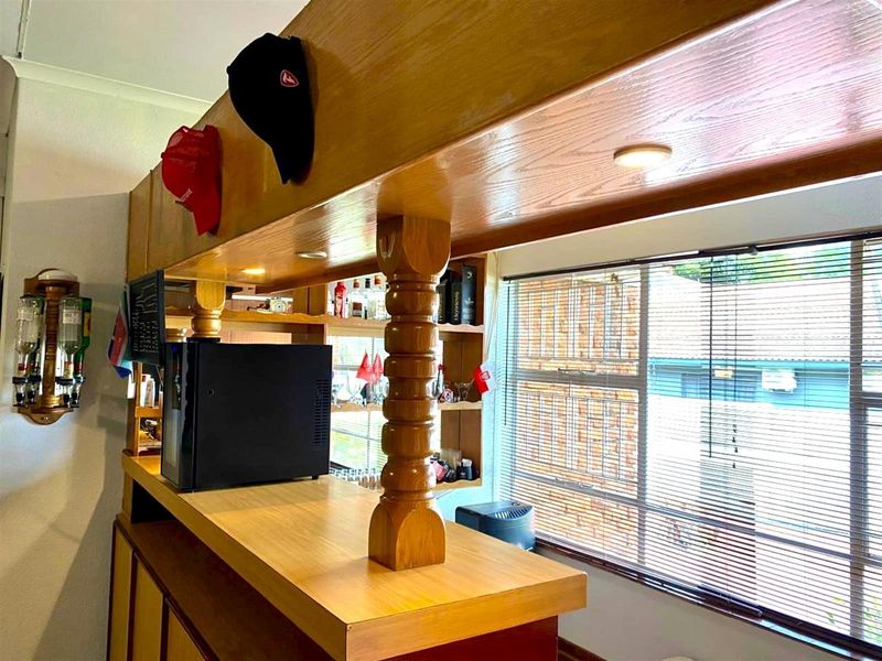 A dedicated home bar area featuring a built-in timber counter, integrated shelving, and natural light through large windows with venetian blinds.