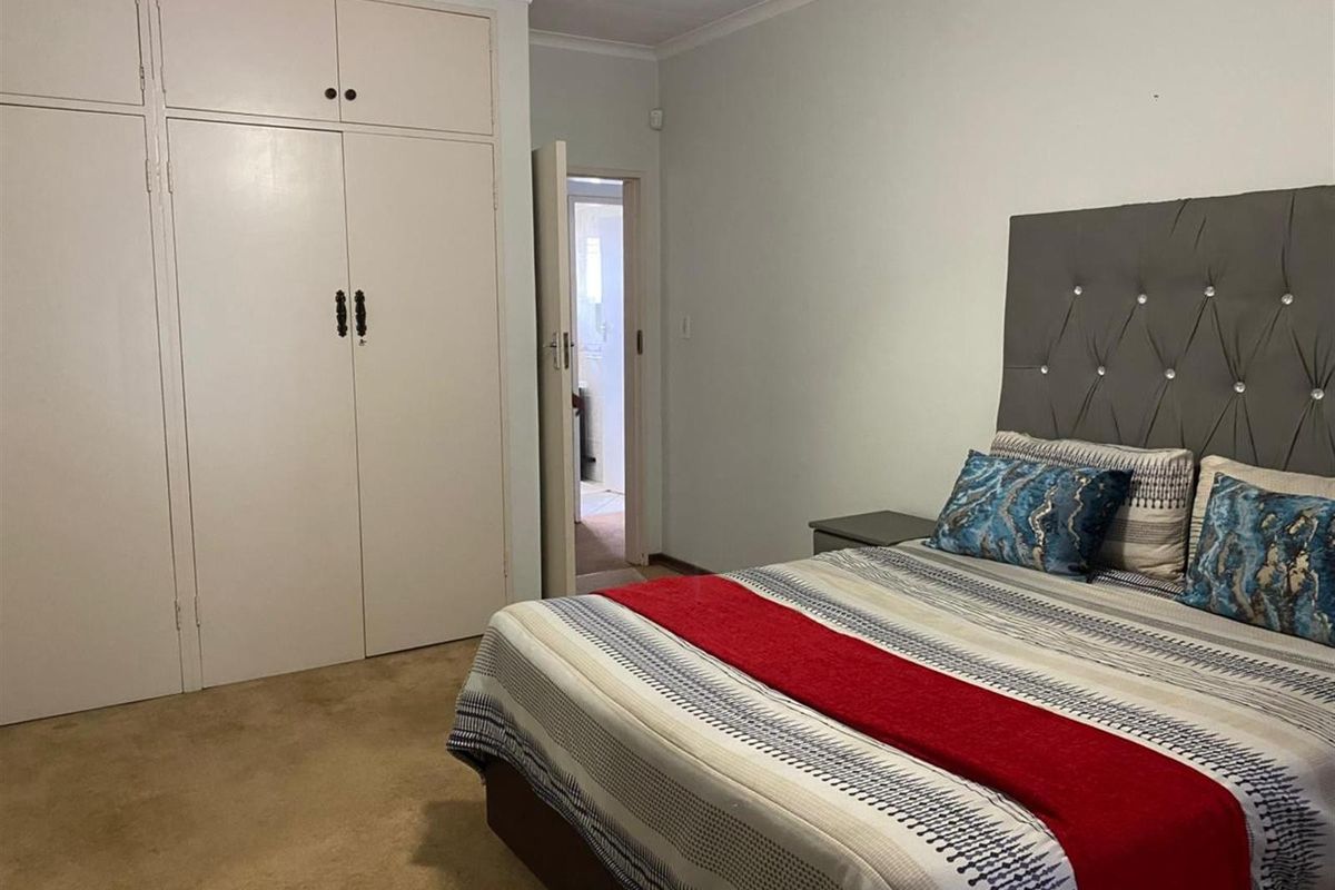 A functional bedroom featuring built-in cupboards and direct access to an adjoining bathroom, finished with neutral walls and carpeted flooring.