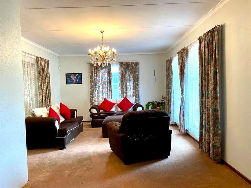 A spacious living room featuring a classic chandelier, coved ceilings, and wall-to-wall carpeting, offering a comfortable and traditional living space.