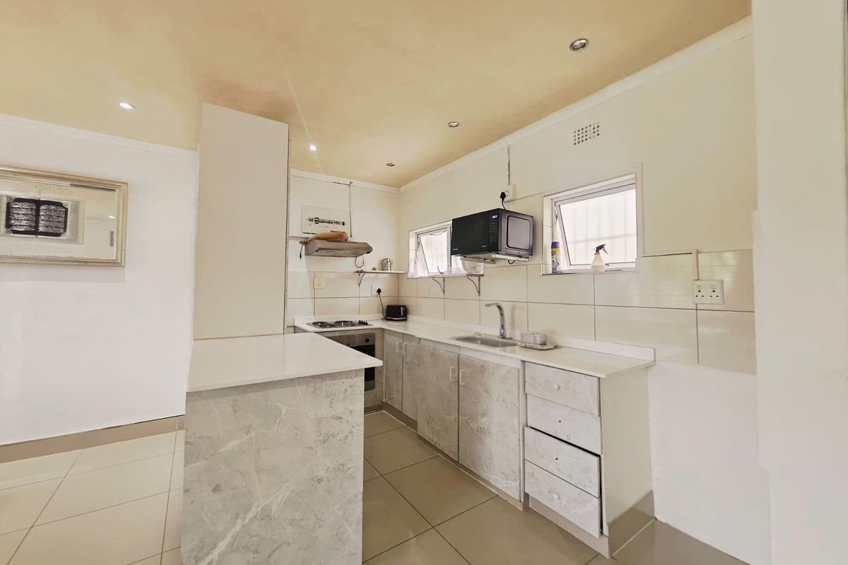 Compact kitchen featuring marble-look cabinetry, stone countertops, stainless steel sink, built-in oven, and extractor fan with tiled splashbacks and floor.