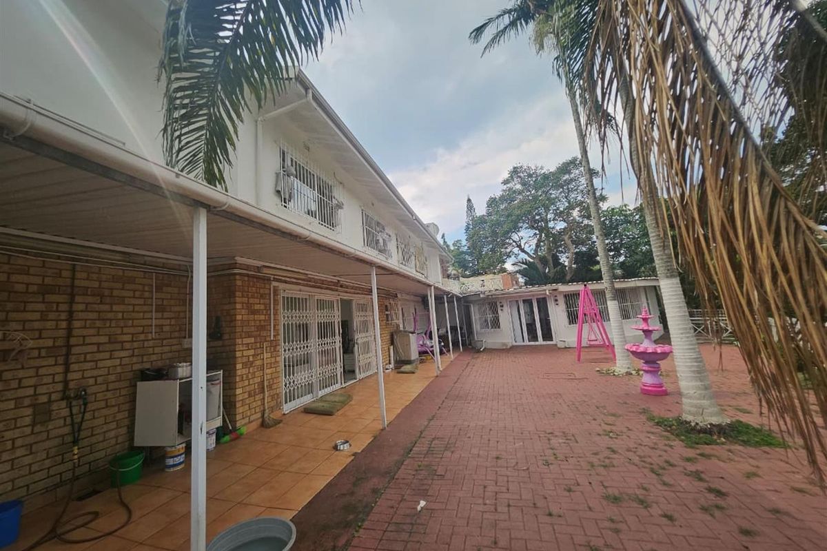 Spacious rear exterior featuring a covered patio area, brick paving, and established palm trees, providing a functional outdoor space for relaxation and entertainment.