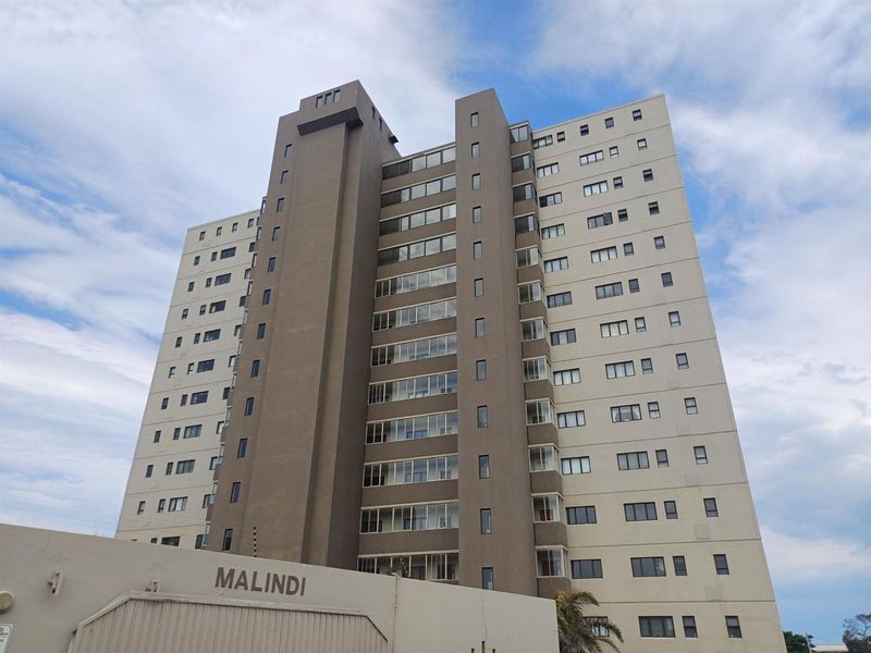 A low-angle exterior view of the Malindi apartment building, showcasing its multi-story concrete facade, uniform window placement, and integrated balcony structures.