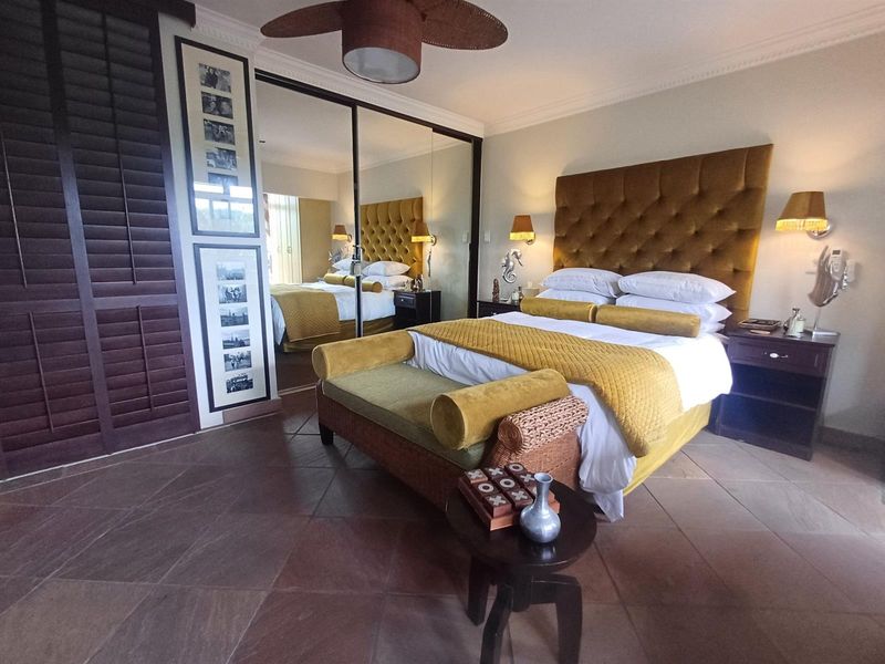 Spacious bedroom featuring stone tile flooring, crown molding, a ceiling fan, and large mirrored sliding wardrobe doors.