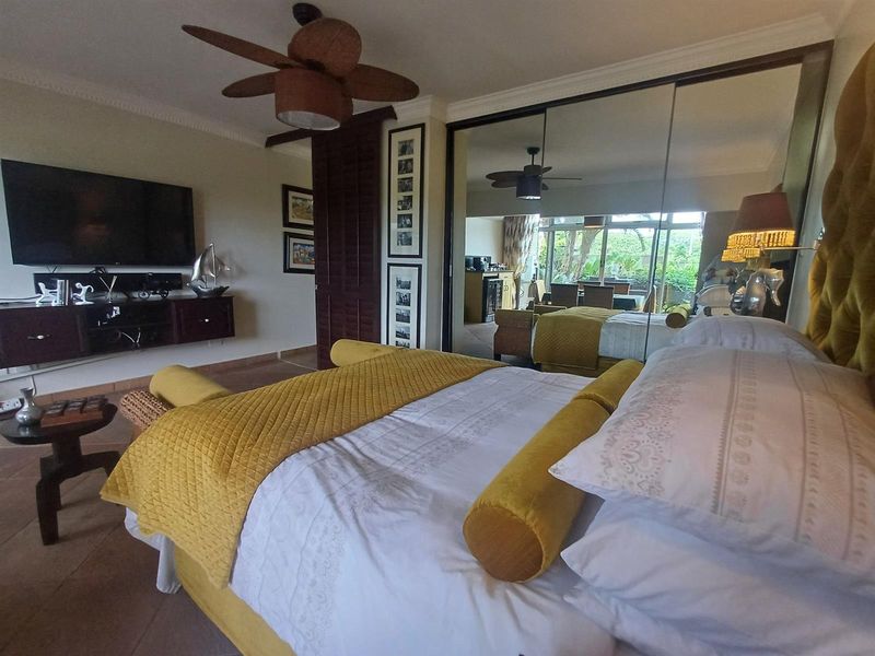 A well-maintained bedroom featuring tiled flooring, crown molding, a ceiling fan, and large mirrored sliding wardrobe doors reflecting the adjacent living space.