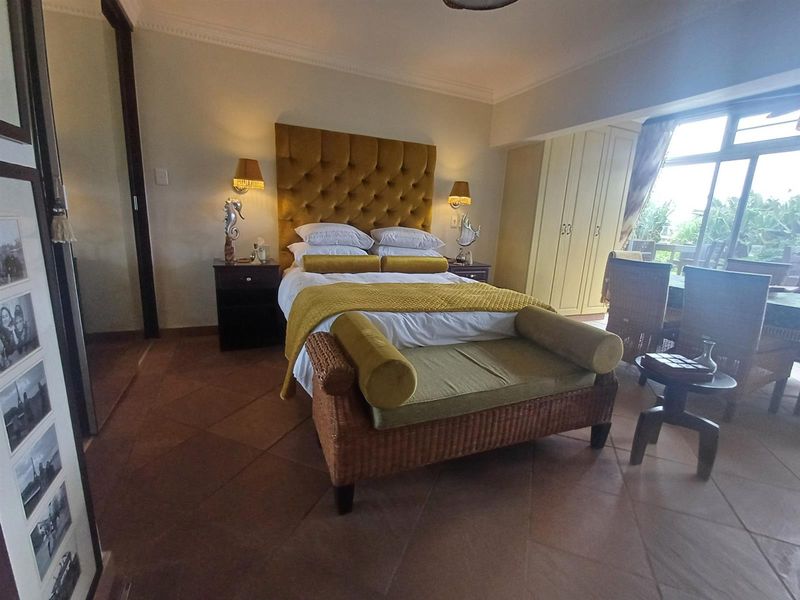 A well-maintained bedroom featuring terracotta floor tiles, built-in cupboards, and direct access to a balcony through sliding glass doors.