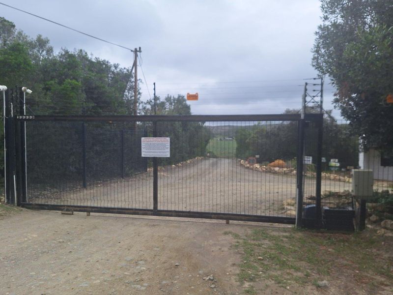 A secure gated entrance to a vacant residential property, featuring a metal mesh sliding gate, electric fencing, and security cameras.