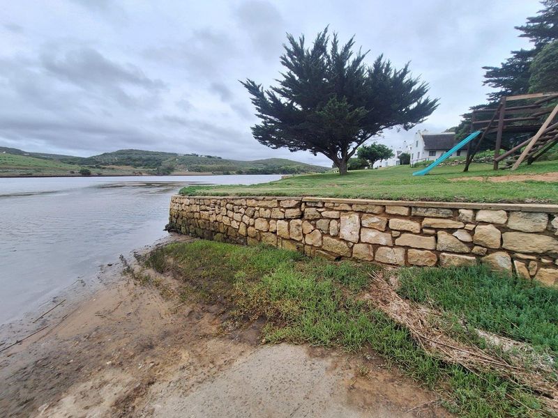 A scenic view of the riverfront property featuring a stone retaining wall, manicured lawn, and mature trees along the water's edge.