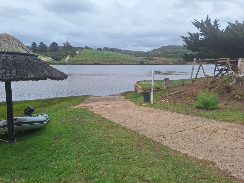 A waterfront view of a residential property featuring a concrete boat ramp, grassed area, and direct access to the water.