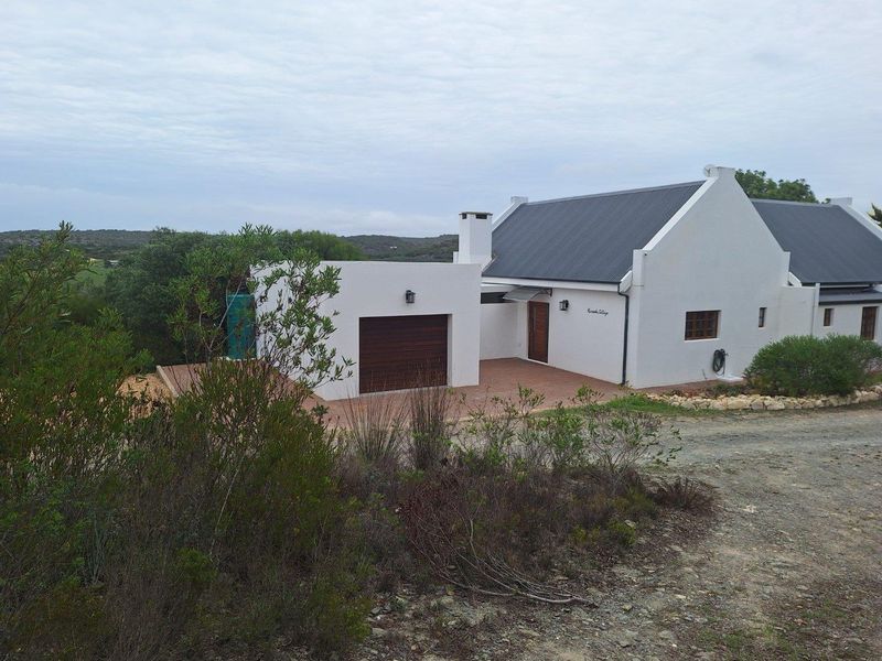 A well-maintained residential cottage featuring a pitched roof, attached garage, and paved driveway, set within a natural landscape.