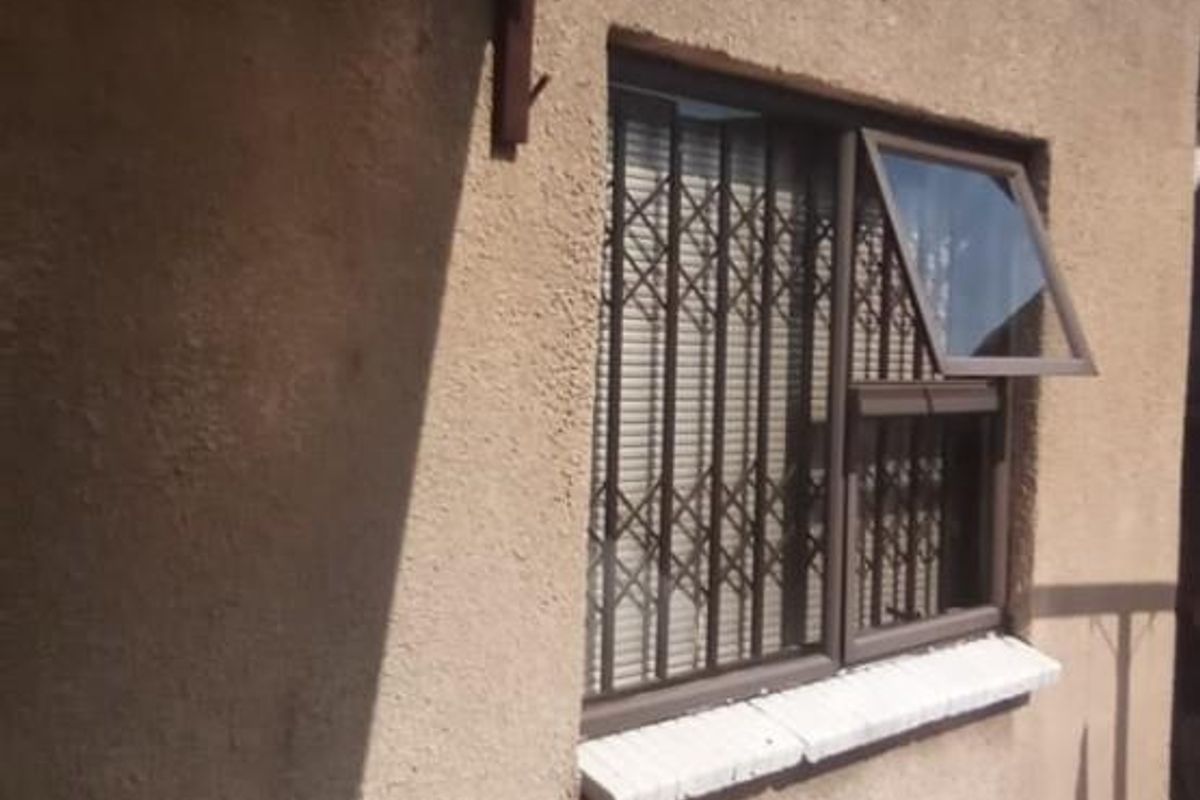 Exterior view of the property showing a textured wall finish, security bars on the window, and a covered patio area.