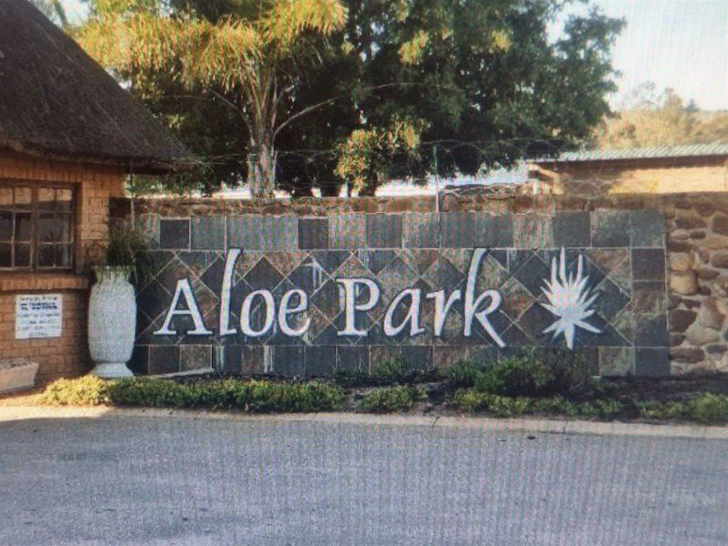 Entrance signage for Aloe Park featuring a stone-clad wall, thatched roof structure, and perimeter security fencing.