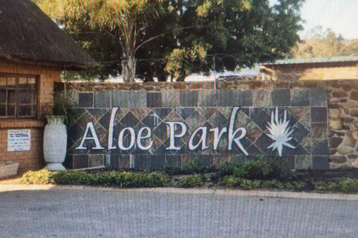 Entrance signage for Aloe Park featuring a stone-clad wall, thatched roof structure, and perimeter security fencing.