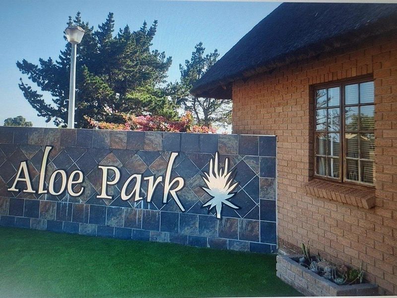 Entrance signage for Aloe Park featuring a stone-clad feature wall, brick masonry, and a thatched roof structure.