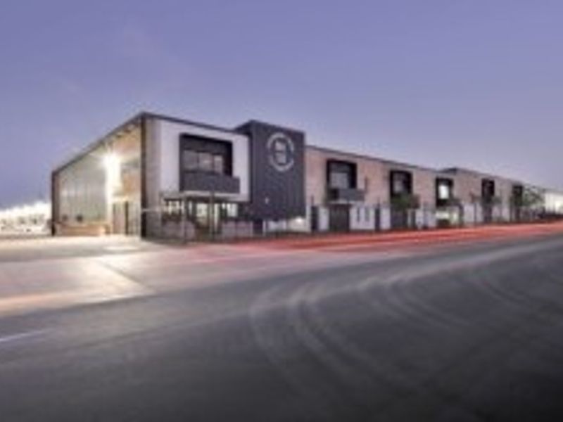 A modern industrial property featuring a clean facade, paved driveway, and secure perimeter fencing, captured during twilight.