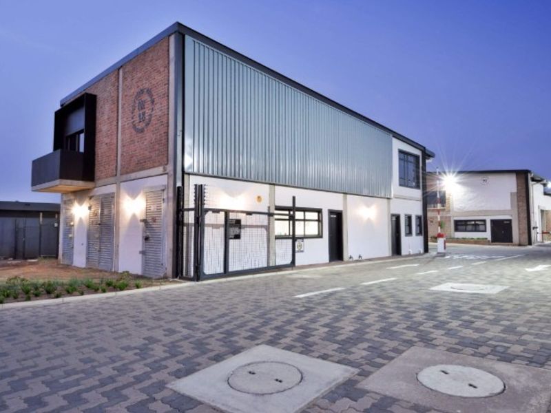 Modern industrial building exterior featuring a combination of brick and metal cladding, secure gated access, and a well-maintained paved driveway.