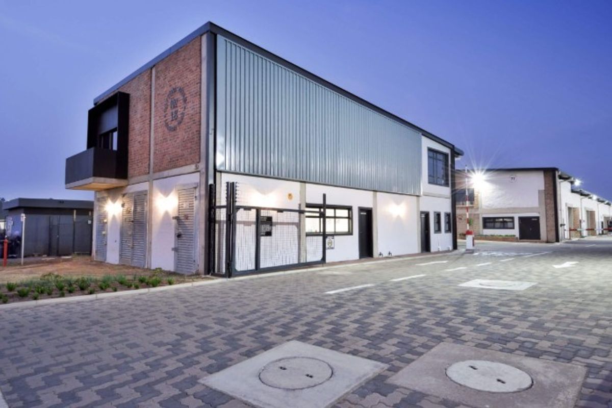 Modern industrial building exterior featuring a combination of brick and metal cladding, secure gated access, and a well-maintained paved driveway.