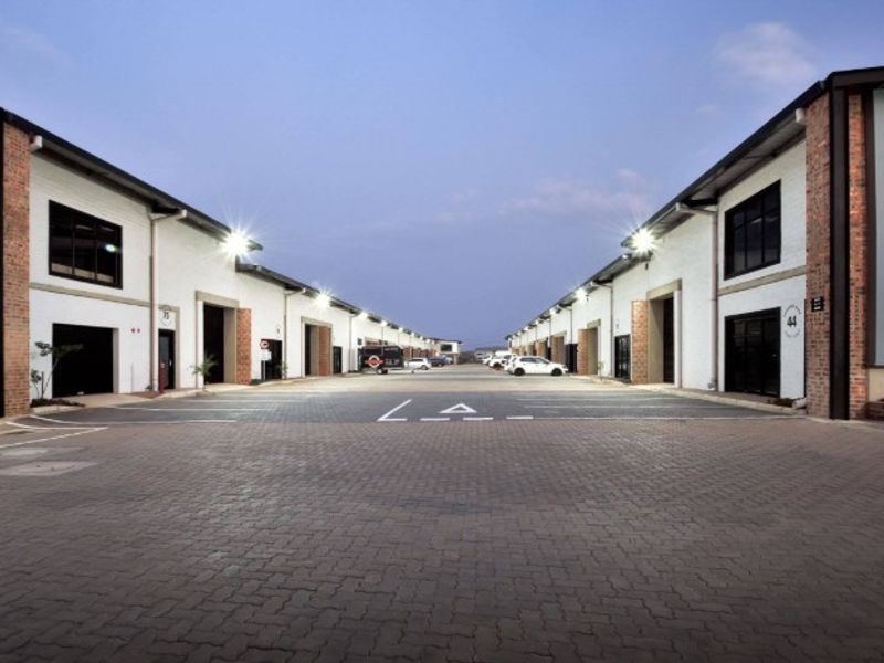 A well-maintained industrial business park featuring a paved central driveway, multiple unit access points with roller shutter doors, and modern exterior lighting.