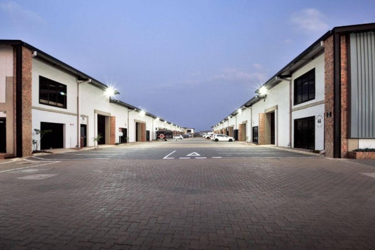 A well-maintained industrial business park featuring a paved central driveway, multiple unit access points with roller shutter doors, and modern exterior lighting.
