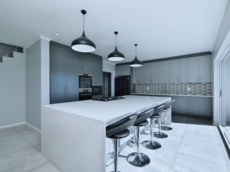 Modern kitchen featuring a large central island with quartz countertops, built-in oven, gas hob, and sleek grey cabinetry with contemporary pendant lighting.