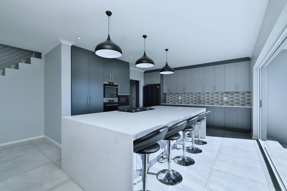 Modern kitchen featuring a large central island with quartz countertops, built-in oven, gas hob, and sleek grey cabinetry with contemporary pendant lighting.