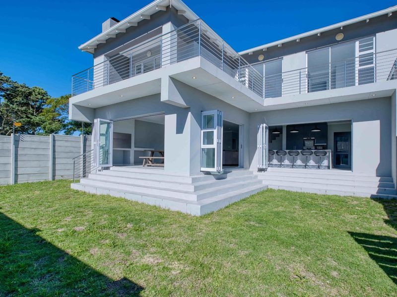 Rear view of a modern townhouse featuring a spacious lawn, raised patio with bi-fold doors, and an upper-level balcony with stainless steel balustrades.