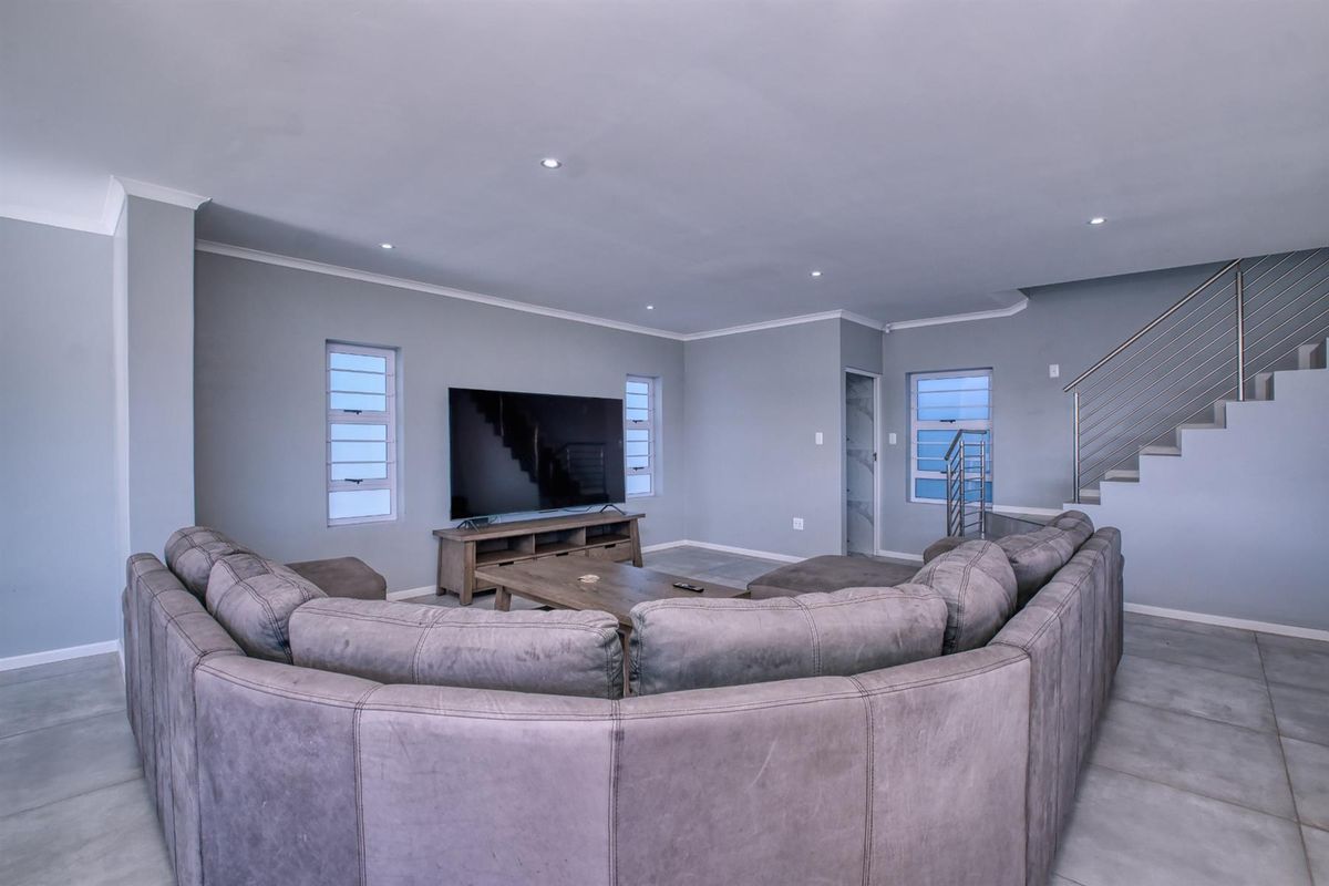 Spacious living room featuring modern tiled flooring, recessed downlights, and a staircase with a sleek stainless steel balustrade.