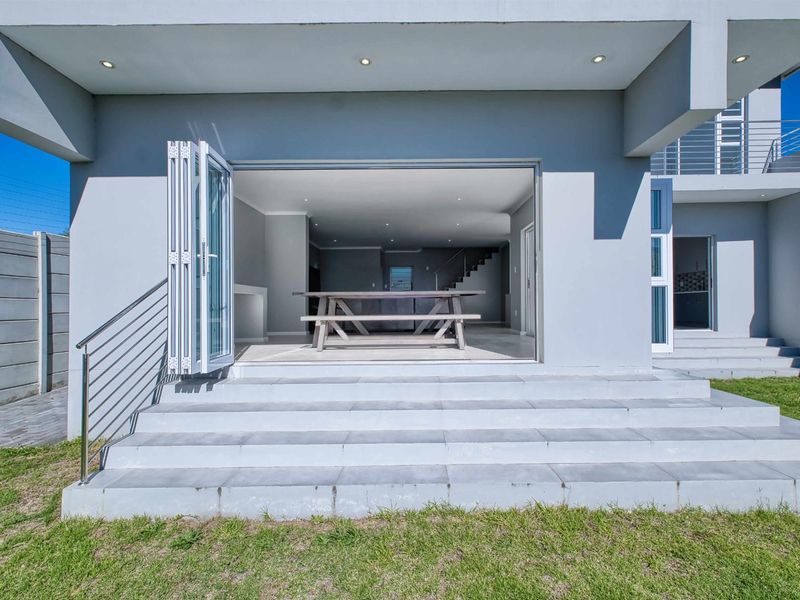 A modern covered patio area featuring wide bi-fold doors leading into the open-plan living space, with concrete steps and stainless steel handrails.