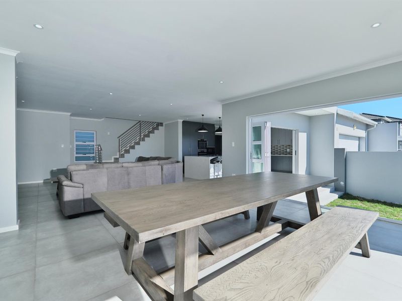 Spacious open-plan living and dining area featuring modern tiled floors, recessed lighting, a sleek kitchen island, and seamless access to the outdoor patio.