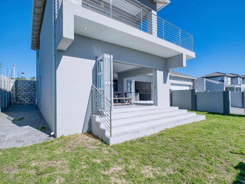 Rear view of the townhouse featuring a paved garden area, concrete steps leading to bi-fold doors, and an upper-level balcony with stainless steel railings.