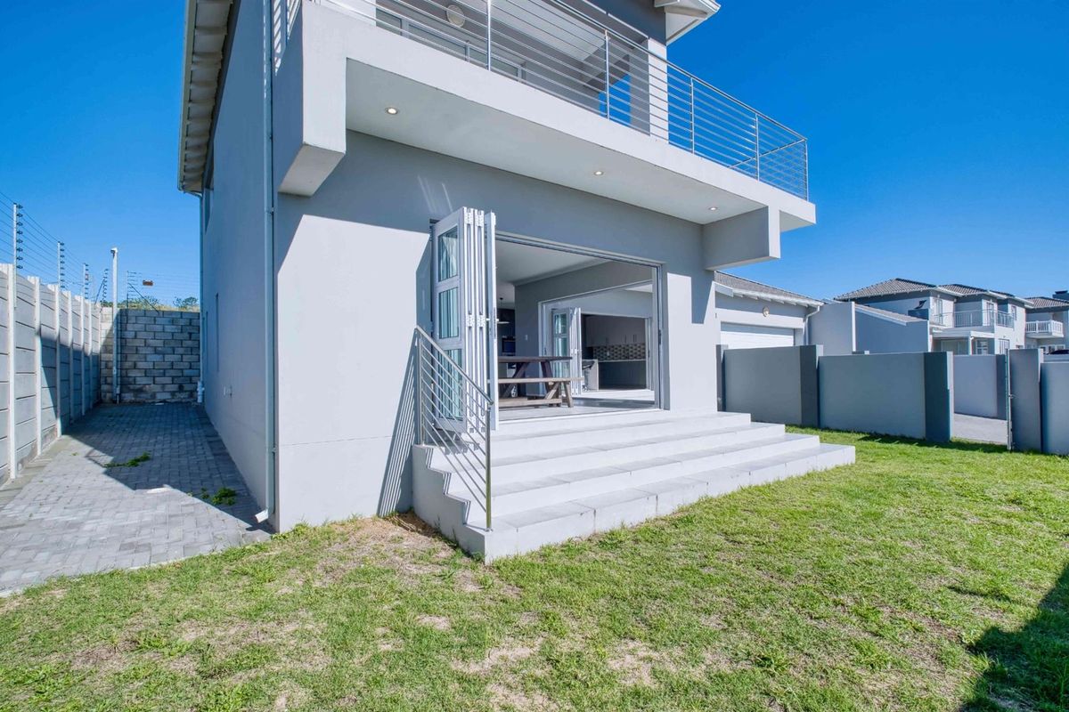 Rear view of the townhouse featuring a paved garden area, concrete steps leading to bi-fold doors, and an upper-level balcony with stainless steel railings.