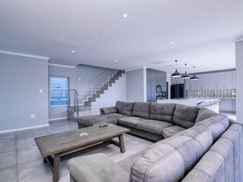 Spacious open-plan living area featuring a modern kitchen with island, sleek cabinetry, built-in appliances, and a staircase with a contemporary metal balustrade.