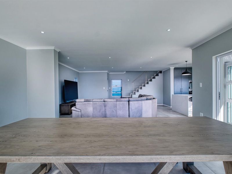 Spacious open-plan living area featuring modern tiled floors, recessed lighting, a sleek staircase, and a contemporary kitchen with a central island.