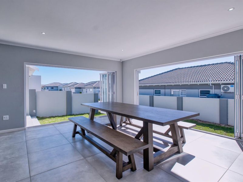 A modern covered patio featuring large bi-fold doors that open to a private garden area, finished with neutral floor tiles and recessed lighting.