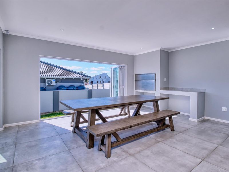 Covered patio area featuring large format floor tiles, a built-in braai, and wide stacking doors opening to the exterior.