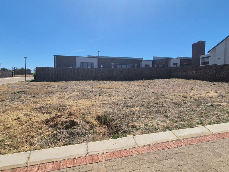 A vacant residential plot featuring a brick boundary wall, situated in a developed neighborhood with paved street access.