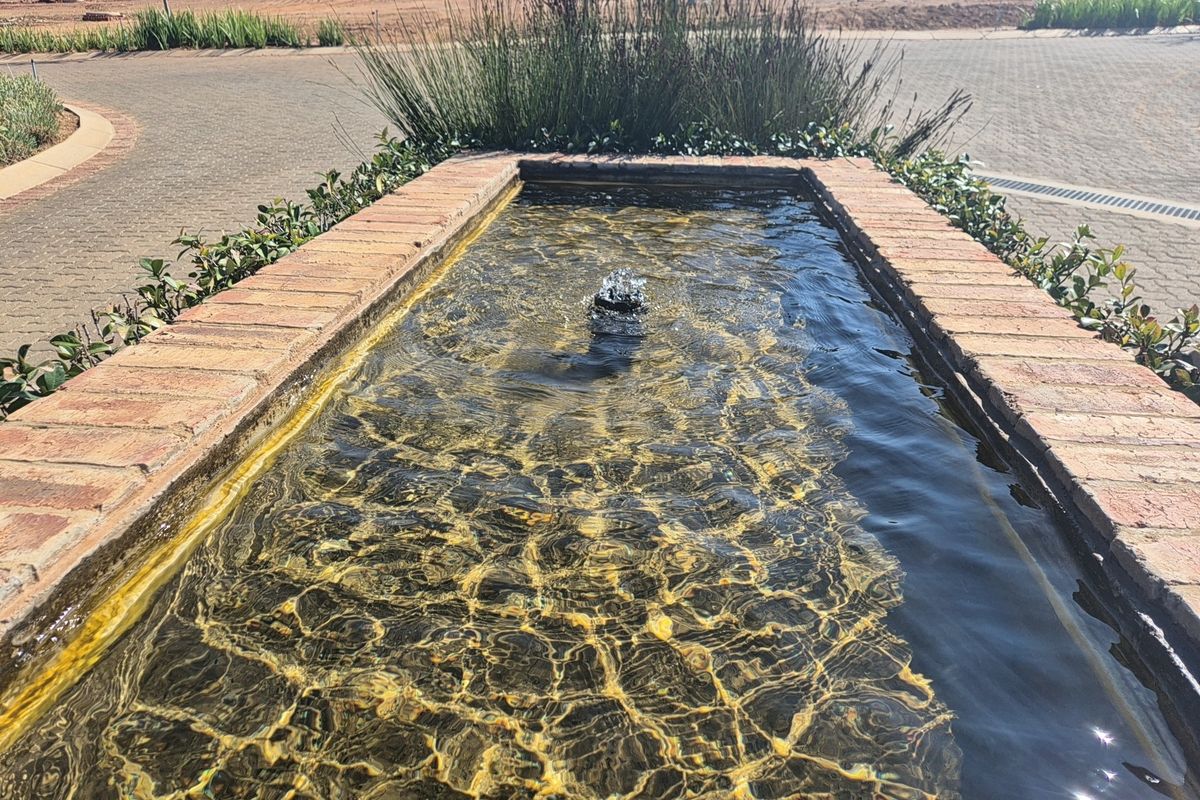 A decorative brick water feature with a central fountain located within a landscaped residential estate area.