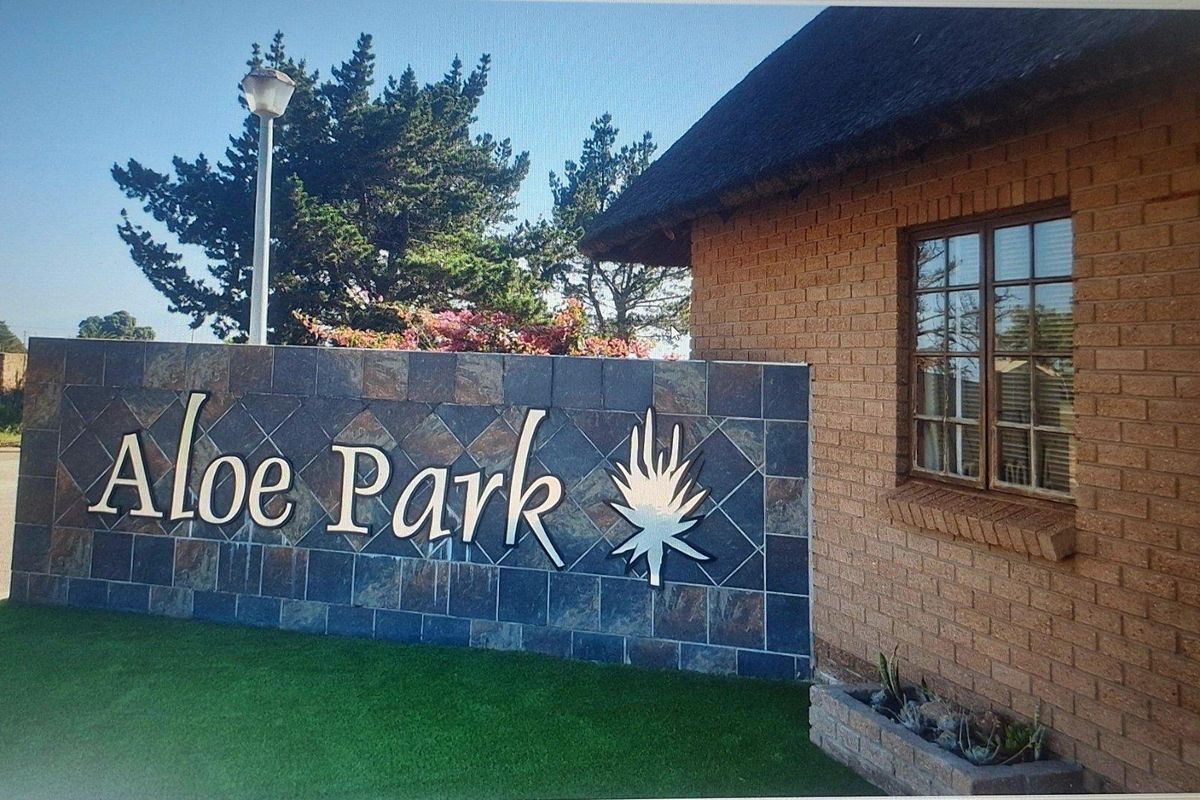 Entrance signage wall for Aloe Park featuring stone cladding, adjacent to a brick building with a thatched roof and built-in planter.