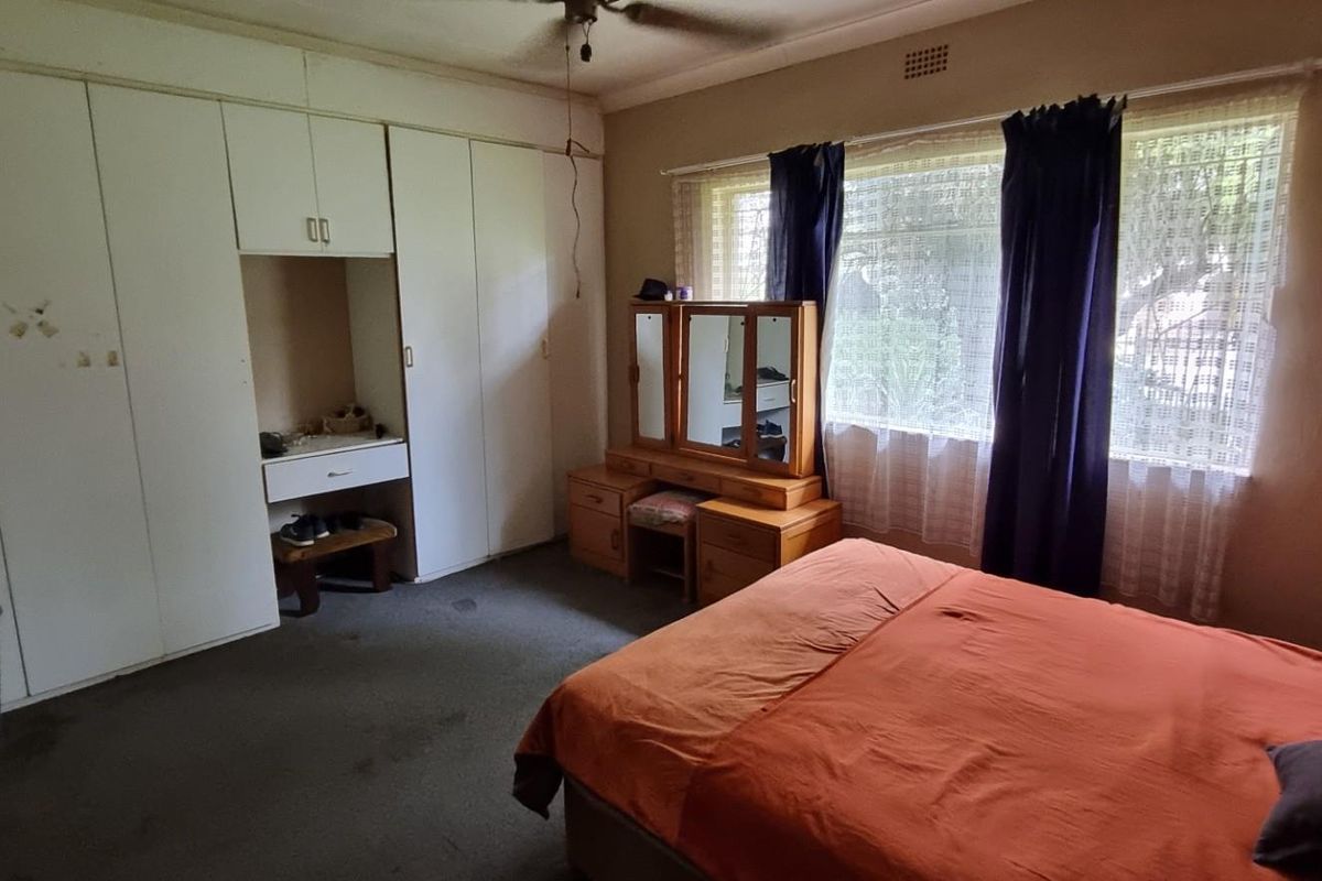 A spacious bedroom featuring extensive built-in cupboards with a central vanity area, large window for natural light, and carpeted flooring.