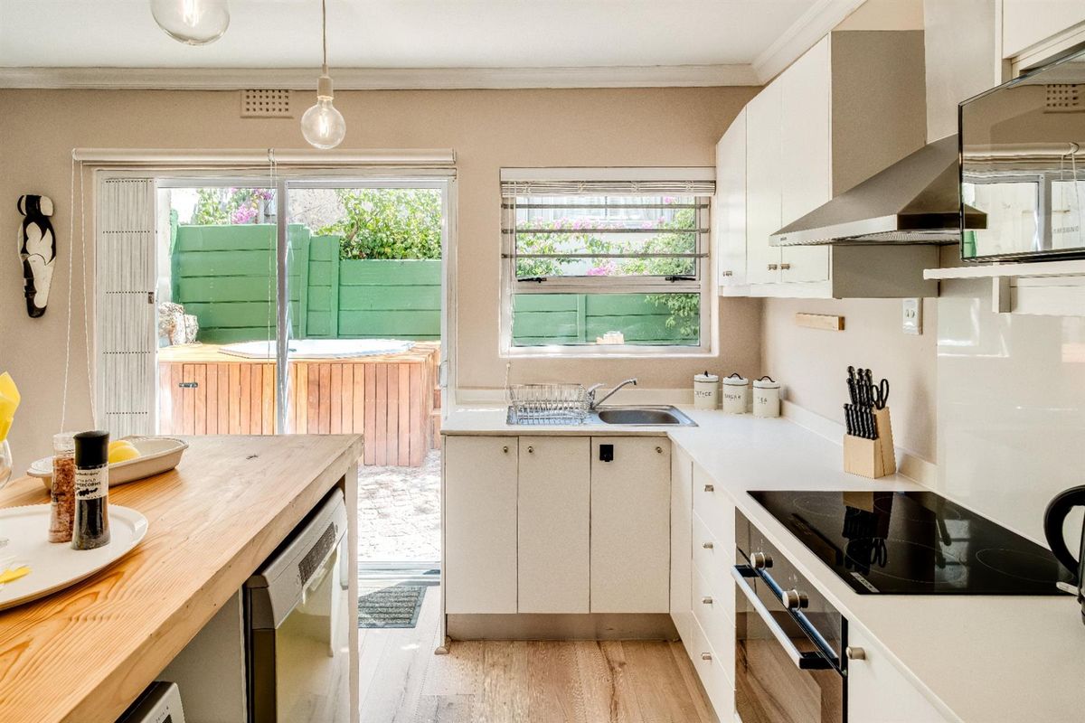 A bright kitchen featuring white cabinetry, a built-in oven and hob, and a wooden breakfast bar, with direct access to an outdoor patio area.