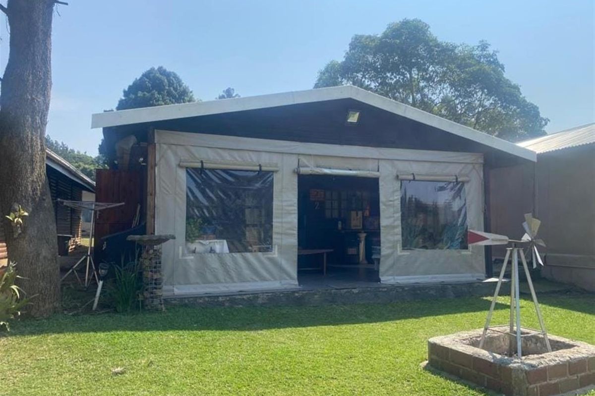 Rear view of the holiday accommodation featuring a covered patio area with canvas enclosures and a brick fire pit in the garden.