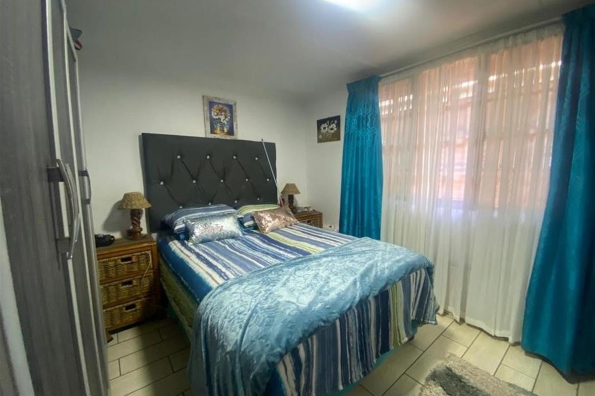 A functional bedroom featuring tiled flooring and a built-in wardrobe, offering a comfortable space with natural light through large window treatments.
