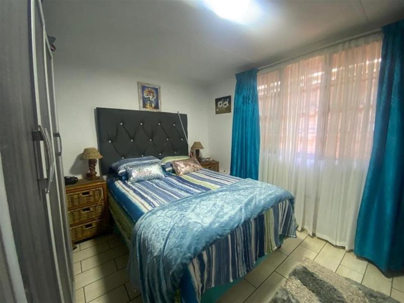 A functional bedroom featuring tiled flooring and a built-in wardrobe, offering a comfortable space with natural light through large window treatments.