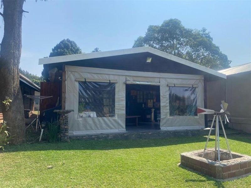 Rear view of the holiday accommodation featuring a timber-clad structure with a canvas-enclosed patio area and a brick fire pit in the garden.
