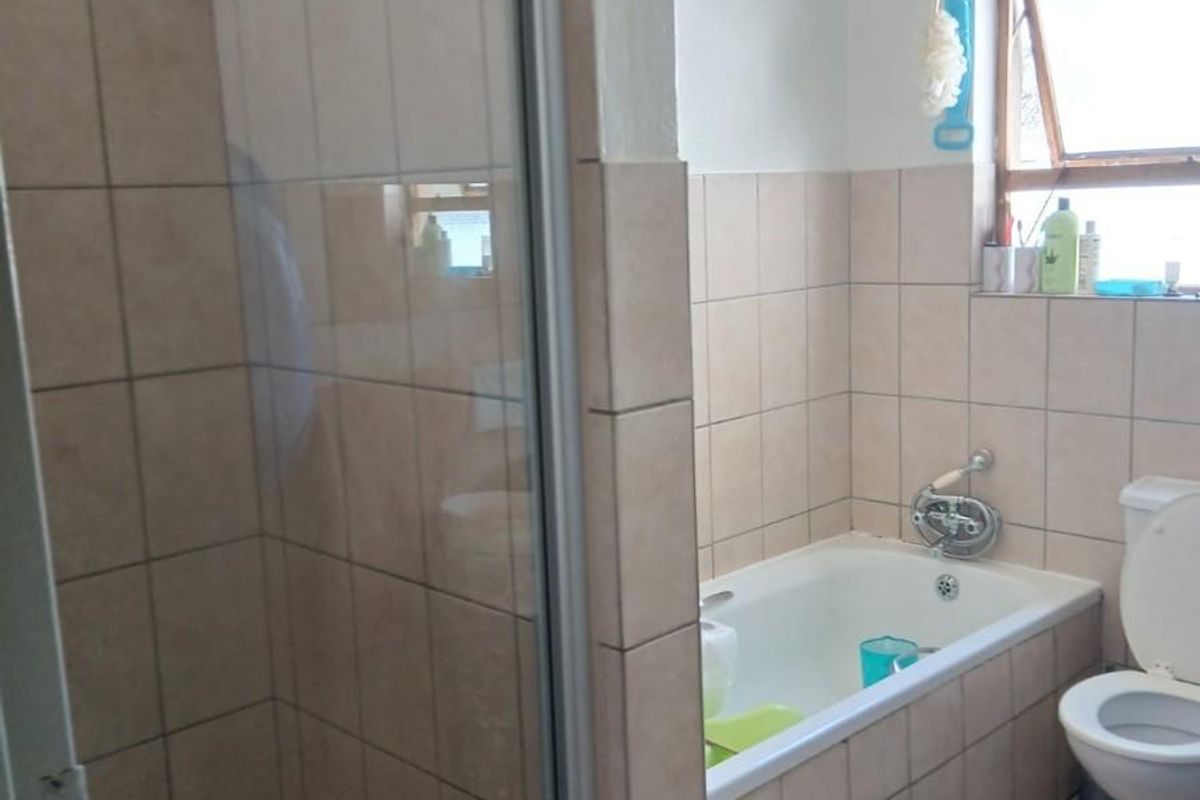 A functional bathroom featuring a tiled shower enclosure, a built-in bathtub with wall-mounted mixer, and a standard toilet.