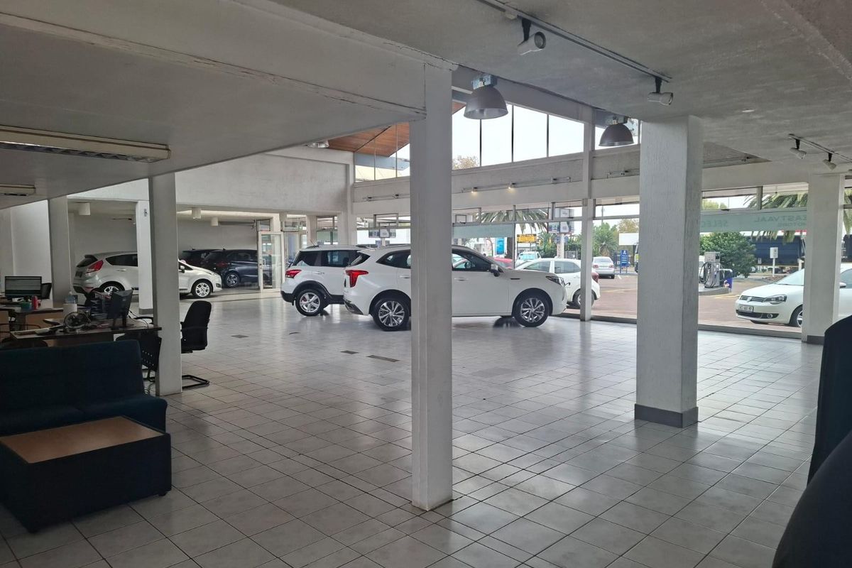 Spacious commercial showroom featuring large glass windows, tiled flooring, and structural support columns, ideal for vehicle display or retail operations.