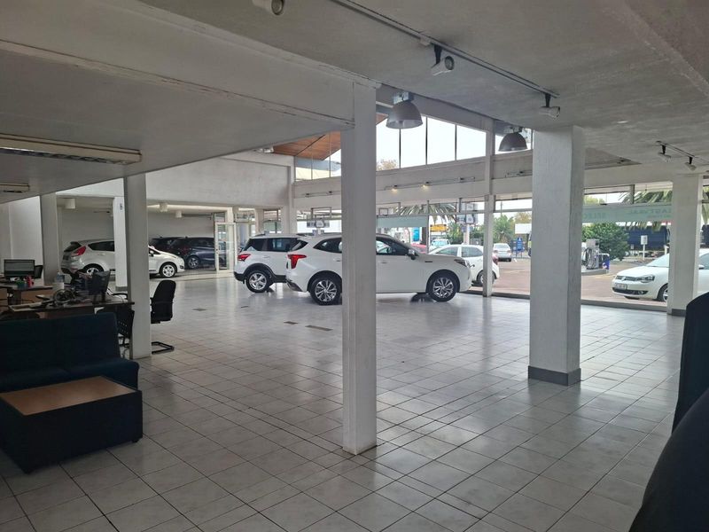 Spacious commercial showroom featuring large glass windows, tiled flooring, and structural support columns, ideal for vehicle display or retail operations.