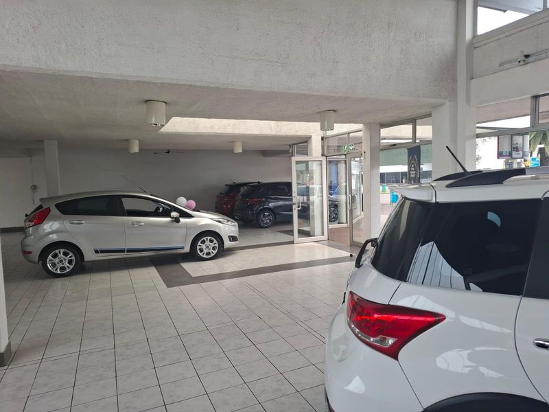 Spacious commercial showroom area featuring tiled flooring, large glass entrance doors, and high ceilings, suitable for vehicle display or retail operations.