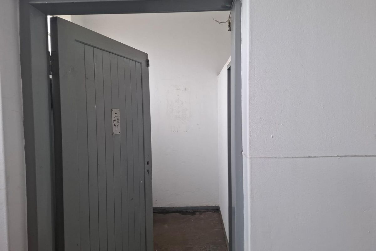 A view into a basic commercial restroom facility featuring a painted timber door with signage and plain interior walls.