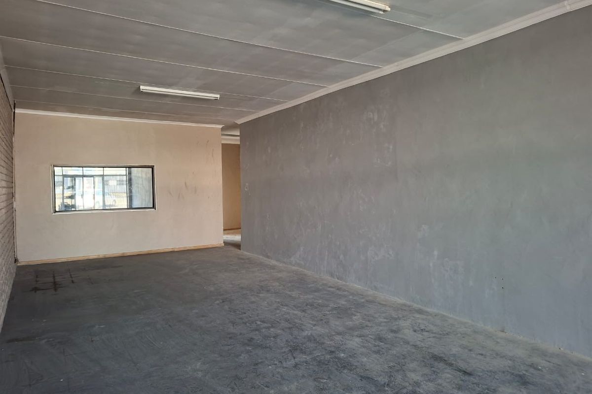 An empty, open-plan commercial space featuring concrete flooring, grey painted walls, and fluorescent lighting, suitable for various business or retail applications.