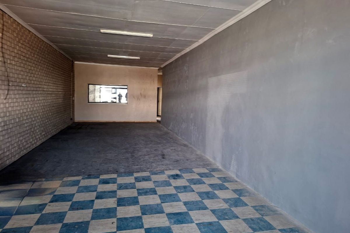 An empty, open-plan commercial space featuring checkered flooring, exposed brickwork, and basic fluorescent lighting, suitable for various retail or office configurations.
